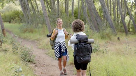 Two-women-are-hiking-on-a-forest-trail,-one-with-a-plaid-shirt-tied-around-her-waist
