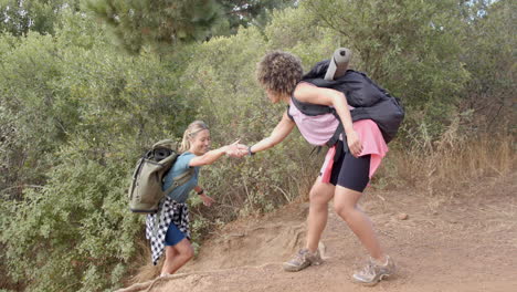 Young-Caucasian-woman-helps-her-biracial-friend-up-a-steep-trail