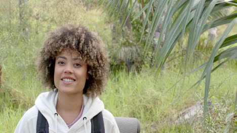 A-young-biracial-woman-with-curly-hair-smiles-in-a-natural-outdoor-setting-with-copy-space