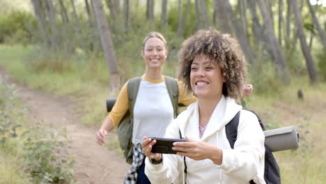 Two-women-enjoy-a-hike-in-a-wooded-area,-one-with-a-phone-in-hand