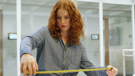 Animation-of-red-shapes-over-caucasian-woman-using-tape-measure-in-office