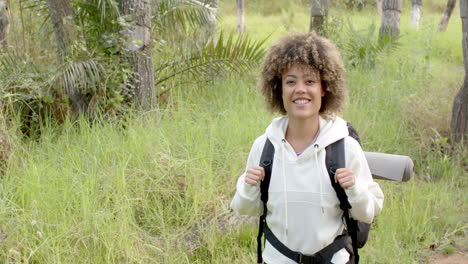 A-young-biracial-woman-with-curly-hair-smiles-while-hiking,-with-copy-space