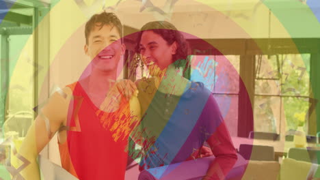 Animation-of-rainbow-rings,-heart-and-stars-over-happy-diverse-gay-male-couple-embracing-at-home
