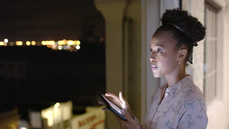African-American-woman-uses-a-tablet-at-night-on-a-balcony,-with-copy-space
