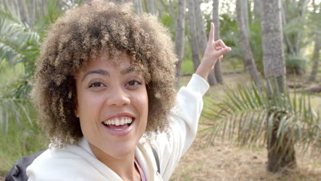 A-young-biracial-woman-with-curly-hair-smiles-brightly,-pointing-upwards