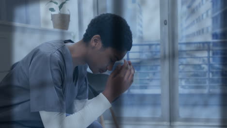 Animation-Von-Regen-Auf-Dem-Fenster-über-Einer-Unglücklichen-Afroamerikanischen-Ärztin,-Die-Den-Kopf-In-Den-Händen-Hält