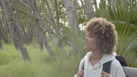 Young-biracial-woman-with-curly-hair-smiles-in-a-forest-setting-with-copy-space