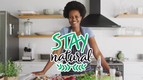 Animation-of-stay-natural-text-over-happy-biracial-woman-with-apron-at-home