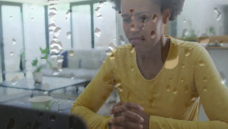 Animation-of-water-droplets-over-unhappy-african-american-woman-sitting-at-home-with-head-in-hands