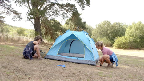 Young-Caucasian-woman-and-biracial-woman-set-up-a-blue-tent-outdoors