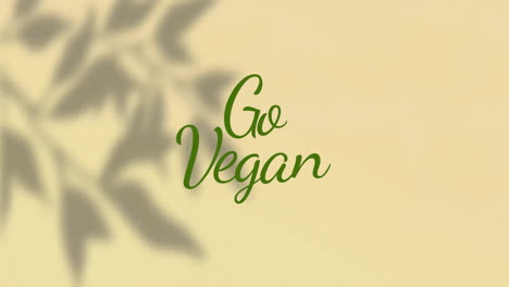 Animation-of-go-vegan-text-over-shadow-of-leaves-on-beige-background