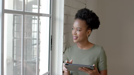 A-young-African-American-woman-holds-a-tablet-near-a-window,-with-copy-space