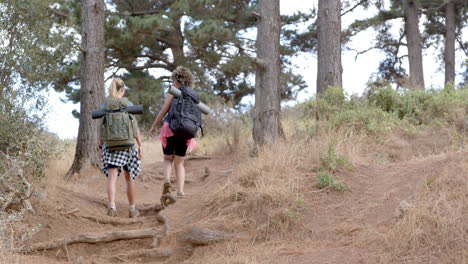 Two-women-hike-on-a-rugged-trail-amidst-trees-and-dry-grass-with-copy-space