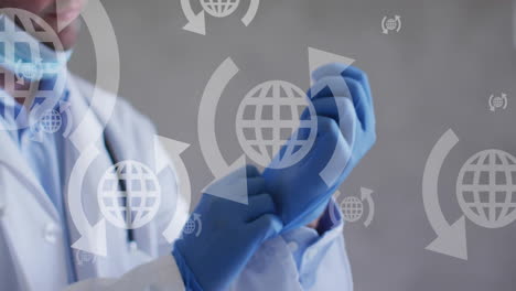 Animation-of-globes-with-arrows-icons-over-caucasian-male-doctor-wearing-rubber-gloves
