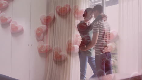 Animation-of-love-text-in-pink-hearts-over-happy-diverse-gay-male-couple-embracing-at-home