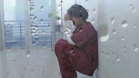 Animation-of-water-droplets-over-unhappy-african-american-female-doctor-crouching-in-corridor