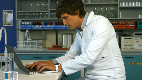 Scientist-using-laptop-while-writing-on-paper