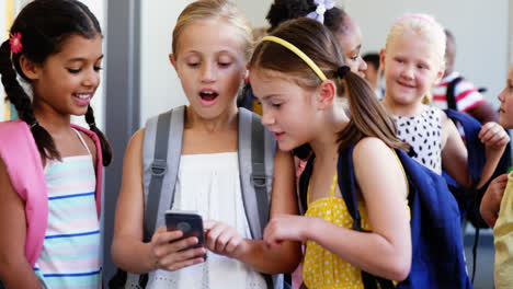 School-kids-using-mobile-phone-in-corridor