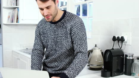 Man-using-laptop-while-having-coffee-in-kitchen