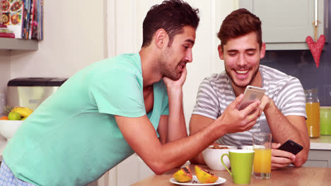 Friends-laughing-while-using-smartphones-in-the-kitchen