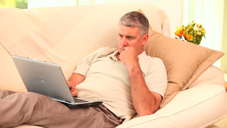Man-lying-on-sofa-using-laptop