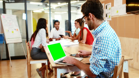 Geschäftsmann,-Der-Laptop-Und-Tablet-Verwendet,-Während-Im-Hintergrund-Ein-Kollege-Eine-Diskussion-Führt