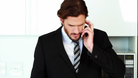 Geschäftsmann-Telefoniert-Mit-Dem-Handy,-Während-Er-In-Der-Küche-Einen-Laptop-Benutzt