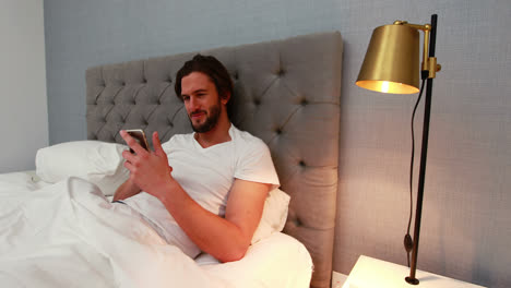 Young-man-using-mobile-phone-in-bed