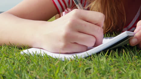 Pretty-young-student-lying-on-the-grass-studying
