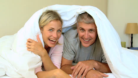 Young-couple-laughing-and-posing-under-the-duvet