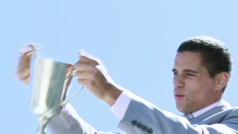 Happy-businessman-holding-a-trophy-outdoors