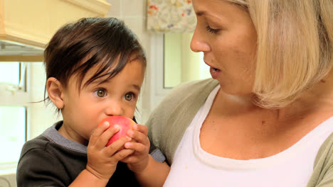 Bebé-En-Brazos-De-La-Madre-Comiendo-Una-Manzana-Roja-