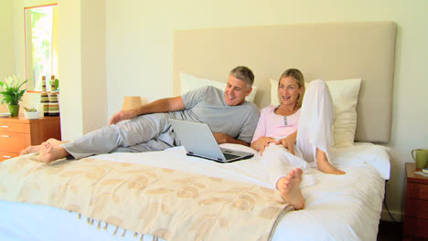 Attractive-couple-relaxing-on-bed-with-laptop