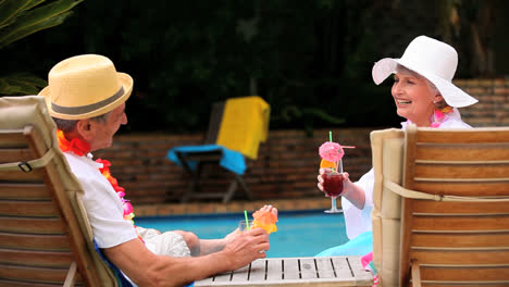 Mature-couple-drinking-cocktails-by-swimming-pool