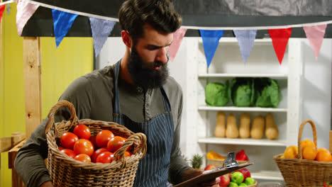 Male-staff-looking-at-checklist-and-holding-a-basket-of-tomatoes