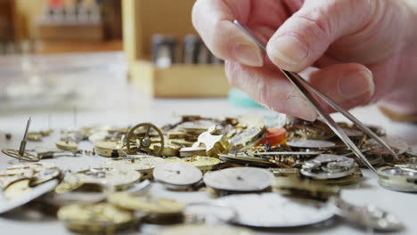Close-up-of-horologist-using-tweezers-to-select-a-watch-part