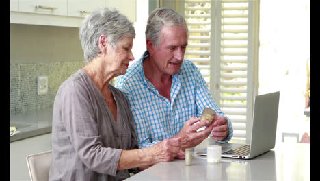 Senior-couple-using-laptop-and-holding-pills