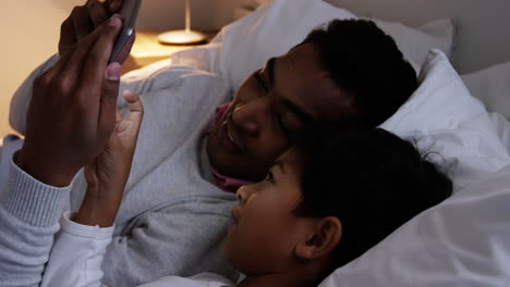 Vater-Und-Sohn-Benutzen-Ein-Digitales-Tablet,-Während-Sie-Auf-Dem-Bett-Liegen