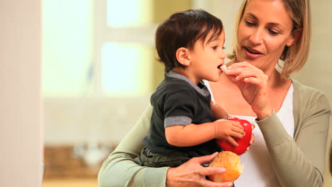 Baby-in-mothers-arms-holding-a-red-pepper-and-eating-bread