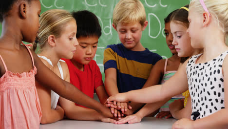School-kids-stacking-hands-in-classroom
