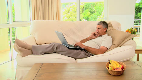 Man-lying-on-sofa-excited-about-something-on-laptop