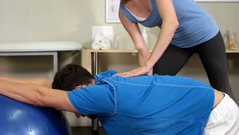 Female-physiotherapist-assisting-man-with-exercise-ball