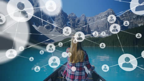 Animation-of-network-of-connections-with-icons-over-caucasian-woman-in-boat-on-lake-in-mountains