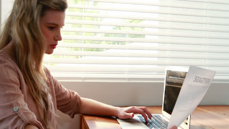 Mujer-Joven-Usando-Una-Computadora-Portátil-Mientras-Mira-El-Documento