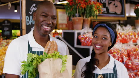 Smiling-staff-holding-basket-and-paper-bag-of-vegetables