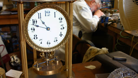 Vintage-torsion-pendulum-clock-on-table-while-horologist-working-in-background