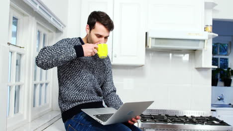 Mann-Benutzt-Laptop,-Während-Er-In-Der-Küche-Kaffee-Trinkt