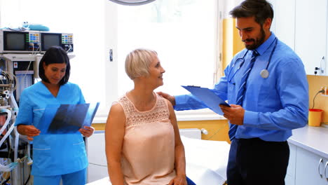 Male-doctor-interacting-with-a-patient-while-nurse-looking-at-x-ray