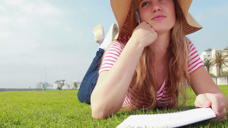 Pretty-young-student-lying-on-the-grass-studying