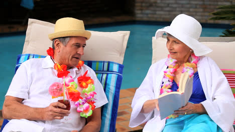 Couple-with-garlands-by-swimming-pool-laughing-over-a-book